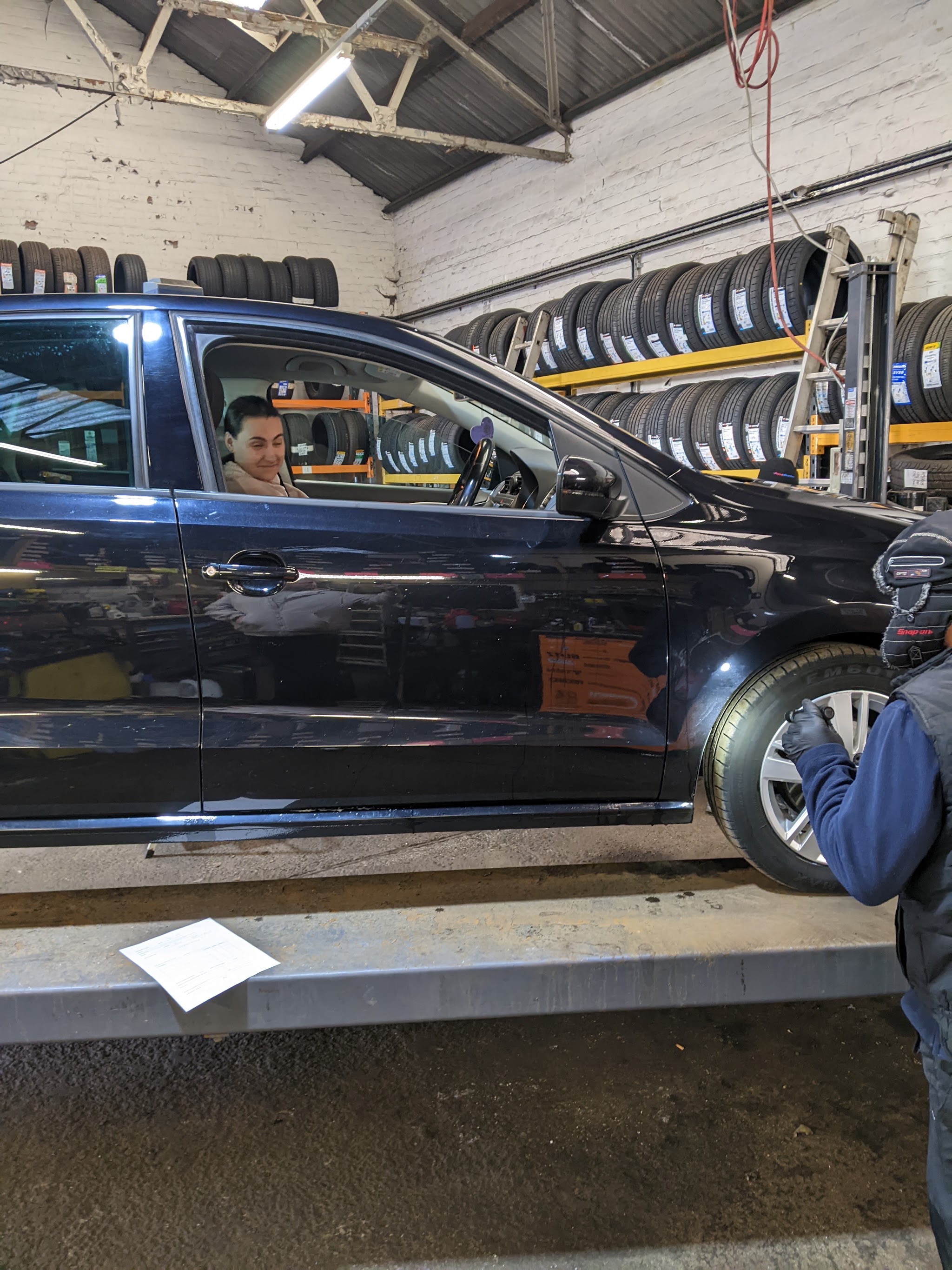 A customer's car up on the ramp in the Cheshire Tyres workshop, with racks of new tyres behind